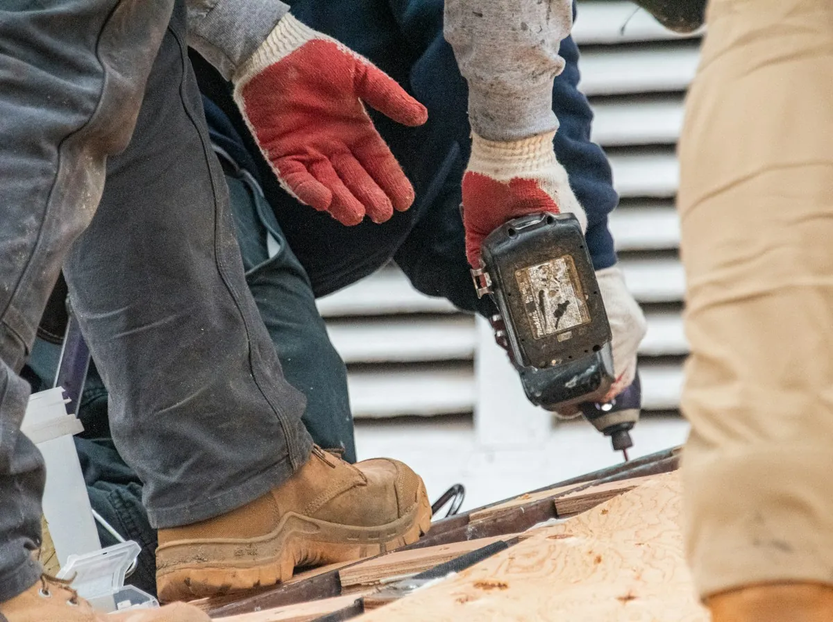 Roof Replacement in Elizabeth — a roofer's boots and gloved hands driving screws with a cordless drill